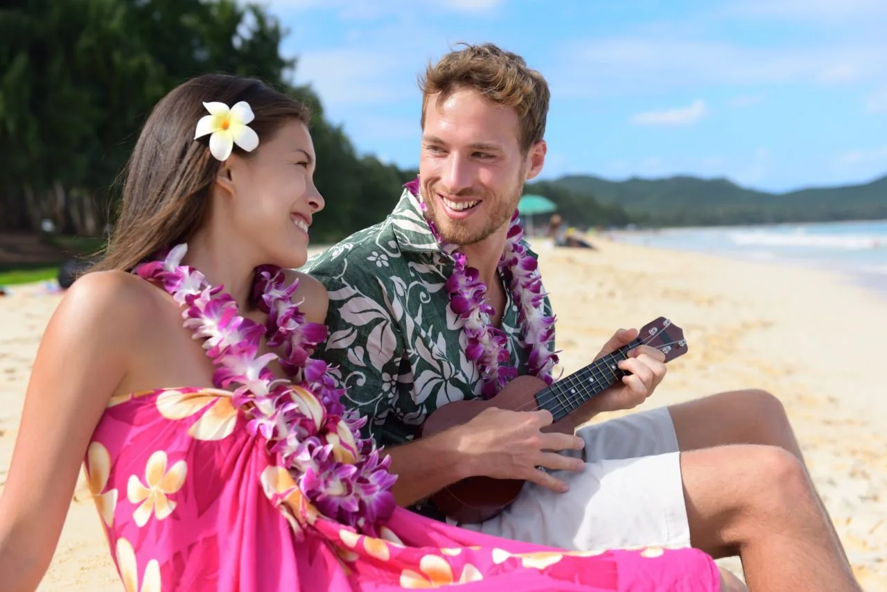 couple honeymooning on a beach in hawaii, man playing ukulele 