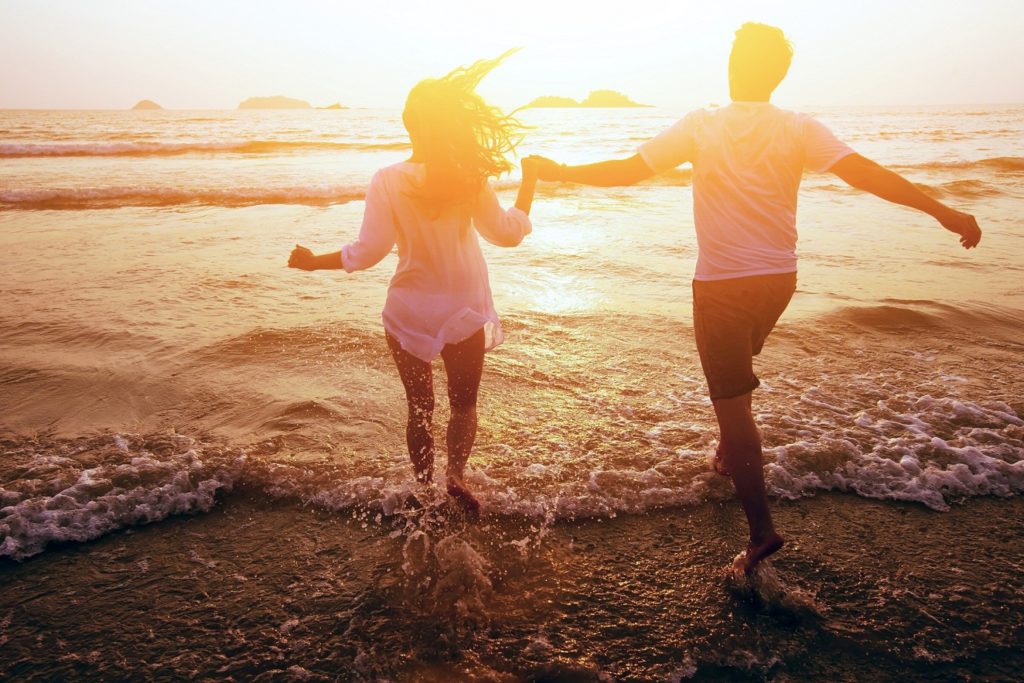 A couple holding hands and running into the ocean.