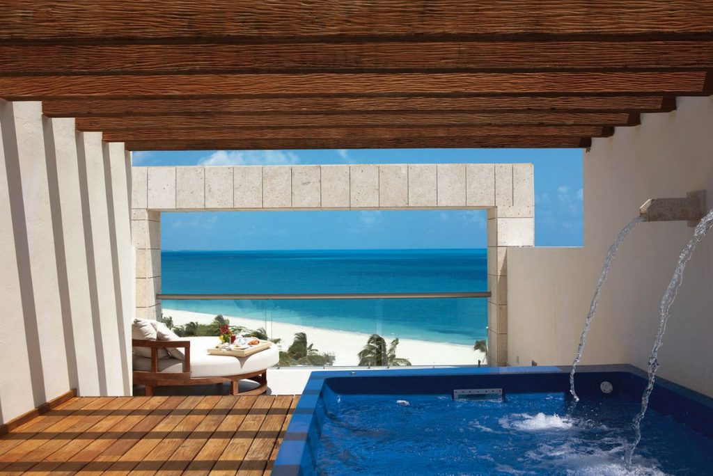 A view of a covered pool overlooking a white, sandy beach and clear, blue water.