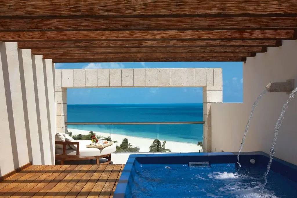 A view of a covered pool overlooking a white, sandy beach and clear, blue water.