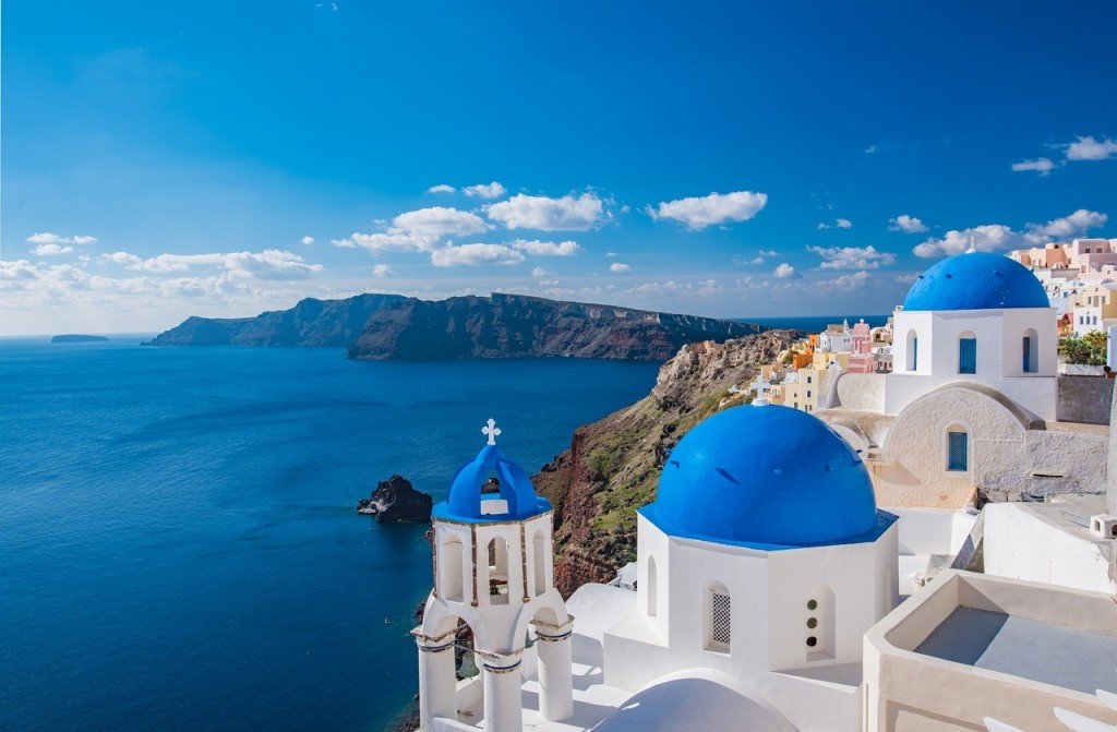 A Greece resort with blue domed roofs overlooking the ocean and mountains.