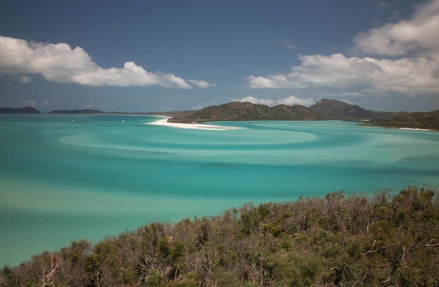 Clear, blue ocean surrounded by hills and green trees.