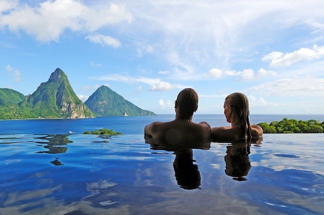 A couple soaking in an outdoor pool overlooking soaring mountains and the ocean.