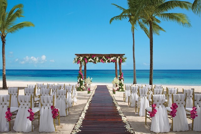 Beach wedding overlooking the ocean with a flower lined walkway and white covered chairs.