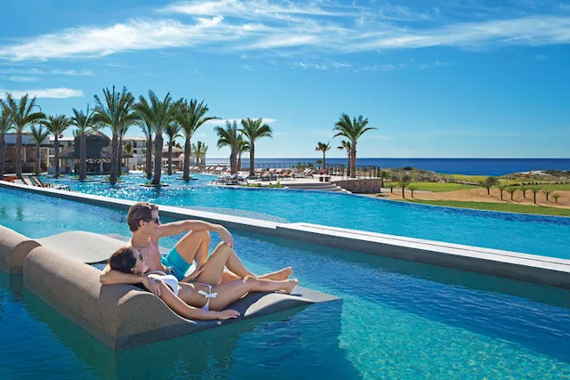 A couple on a lounge chair in a pool at Secrets Puerto Los Cabos Golf and Spa Resort