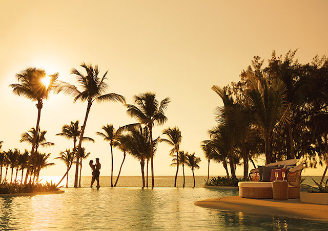 A sunset over a resort pool with a couple in the distance silhouetted and embracing.