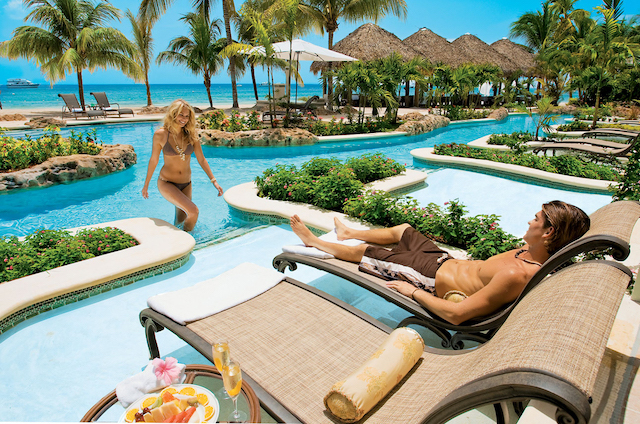 A woman walking out of a pool to a man lounging on a lounge chair.