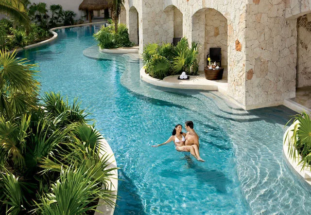 A man holding a woman in a pool just outside the room of a Caribbean luxury resort.