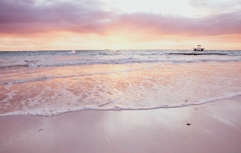 Ocean waves rolling onto a beach as the sunsets in gold and pink.