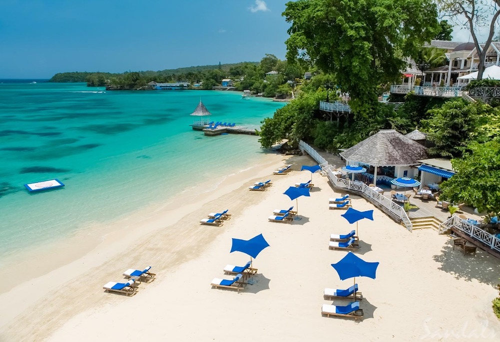 A beach side resort with lounge chairs and blue umbrellas on the sandy shoreline.
