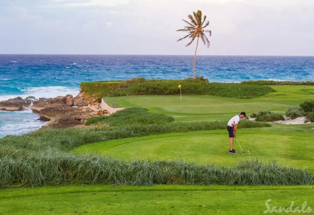 Sandals Emeralds Bay Golf, Tennis and Spa Resort - a man golfs a hole overlooking the ocean