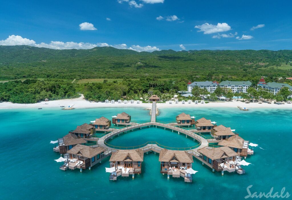 Overwater suites with a heart shaped deck leading back to the beach with lush vegetation.