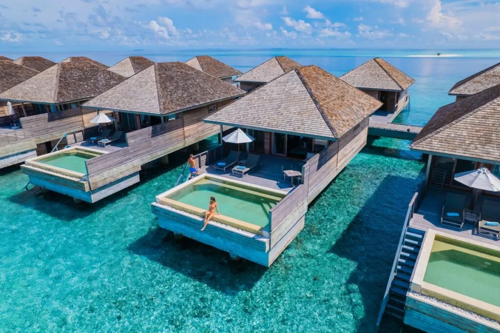 Group of overwater bungalows at Hurawalhi Island Resort with a woman sitting on the edge of a pool.