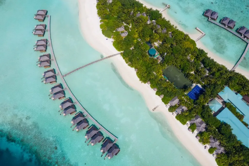 An aerial view of overwater bungalows connected to a lush green island with long boardwalks.