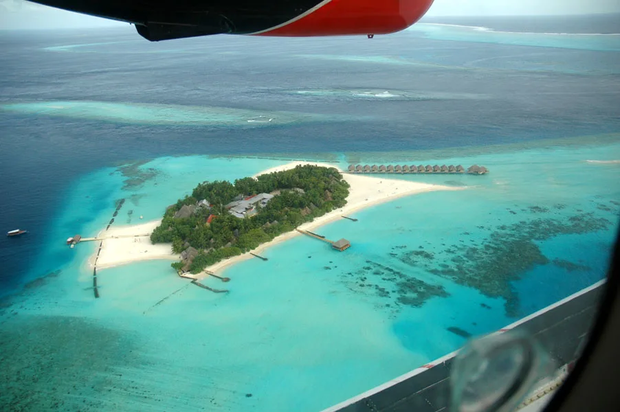 Arial view of an island from a plane. The island has multiple groups of overwater bungalows.