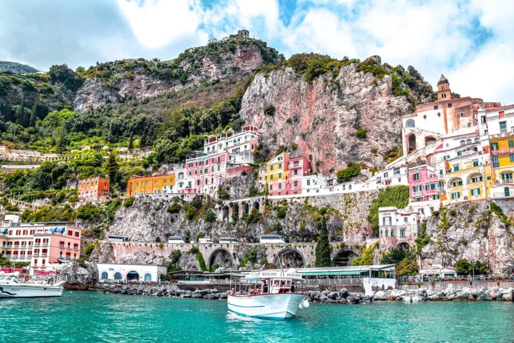 The Amalfi Coast with a boat in clear, blue water and couildings on the cliff side.