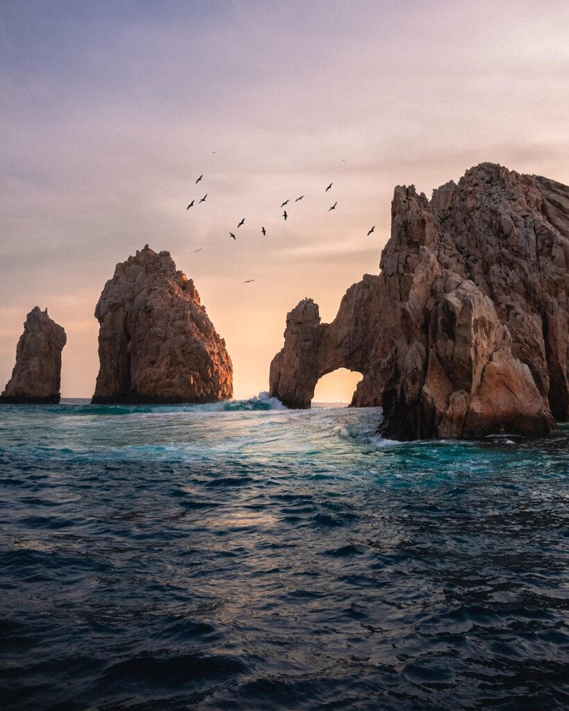 Large rock formations rising out of the ocean with birds in the air.