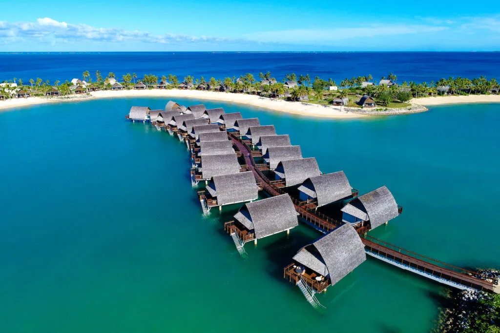 Overwater bungalows at Marriott Momi Bay Resort and Spa, Fiji Islands with beach and trees in the background.