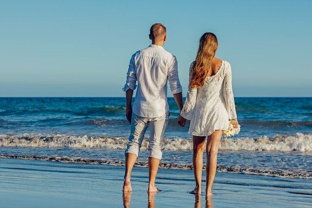 Couple walking hand in hand on the beach with waves in the background.