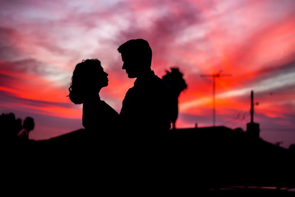 Silhouette of a couple looking at each other with a red and purple sunset in the background.