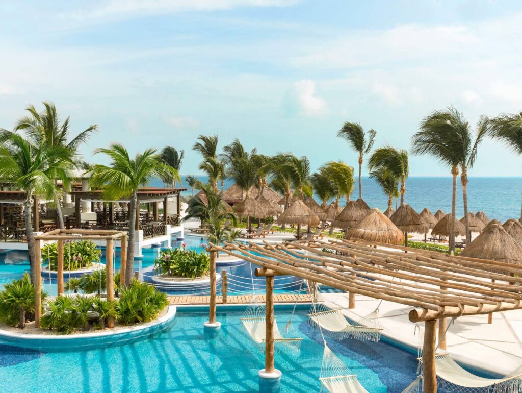 A resort pool with handing hammocks and thatched umbrellas.