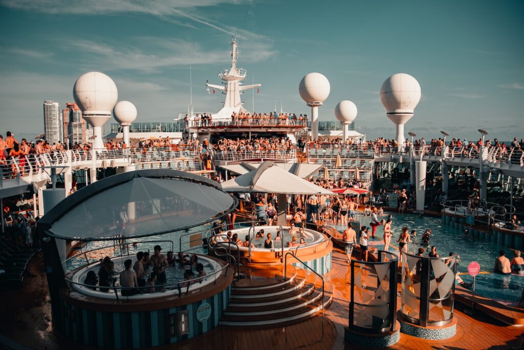 View of the deck of a large cruise ship filled with people, pools, and hot tubs.
