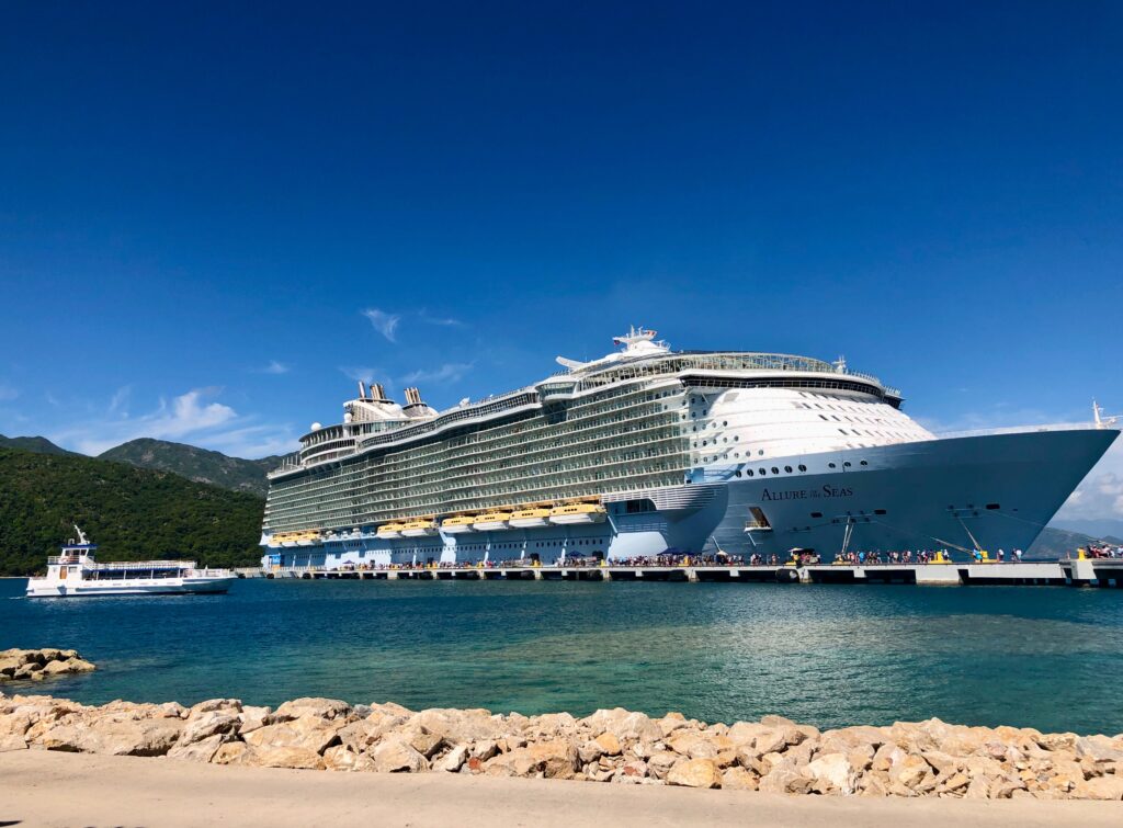 Large cruise ship docked with mountains in the background.