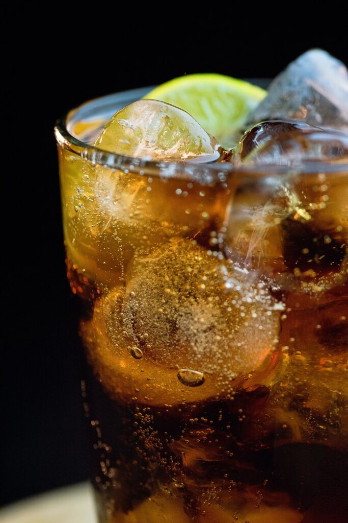 Glass of a dark carbonated beverage with ice and a lime wedge.