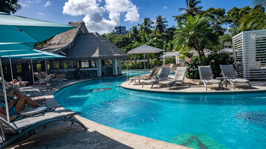 Pool at Sandals Halcyon surrounded by lounging chairs, umbrellas, and lush plants.