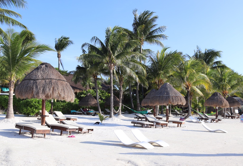 A beach with lounge chairs and thatched umbrellas.